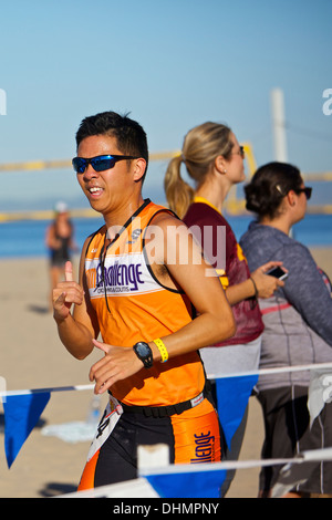 Sorridente americano cinese atleta maschio avvicinando al traguardo a Hermosa Beach Triathlon 2013, Los Angeles, California. Foto Stock