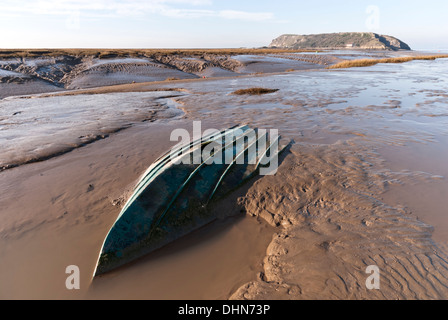 Appartamenti di fango in salita lungo il fiume Ax con una piccola barca affondata nel pericoloso Severn Estuary fango, Brean giù nella distanza. Foto Stock