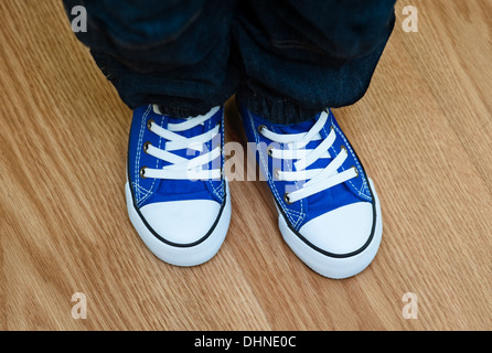 Le gambe di un giovane ragazzo in sneakers sul pavimento a casa Foto Stock