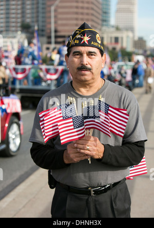 Maschio militare ispanico veterano contiene numerose piccole bandierine americane durante un veterano del giorno parade di Austin in Texas Foto Stock