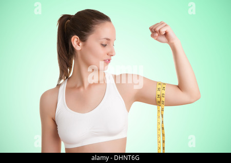 Potente donna misurando il suo bicipite con un giallo nastro di misurazione in uno sfondo verde Foto Stock