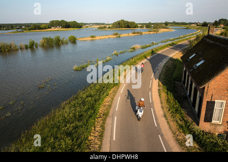 Paesi Bassi, Lienden, Donna in bicicletta e motocicli su Dyke, dove le pianure alluvionali sono allagate Foto Stock