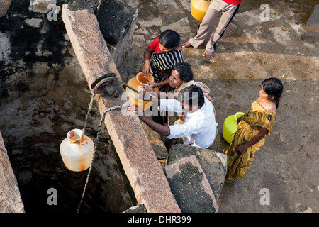 Le donne indiane e gli uomini il prelievo di acqua da un pozzo in una zona rurale villaggio indiano street. Andhra Pradesh, India Foto Stock