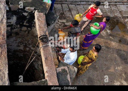 Le donne indiane e gli uomini il prelievo di acqua da un pozzo in una zona rurale villaggio indiano street. Andhra Pradesh, India Foto Stock