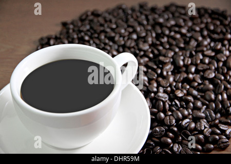 La messa a fuoco delle immagini tazza di caffè e i chicchi di caffè sul tavolo il legno vecchio. Foto Stock