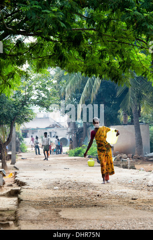 Donna indiana che porta un vaso in materia plastica con acqua da un tubo montante in un territorio rurale villaggio indiano street. Andhra Pradesh, India Foto Stock