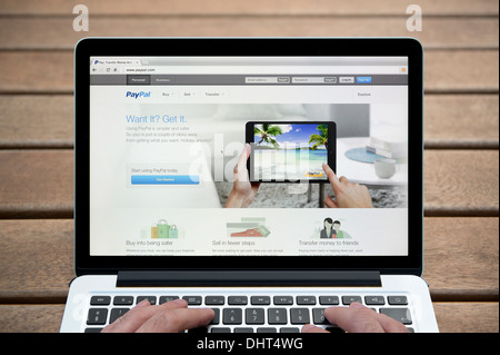 Il sito web di PayPal su un MacBook contro una panca in legno sfondo all'aperto tra cui un uomo le dita (solo uso editoriale). Foto Stock