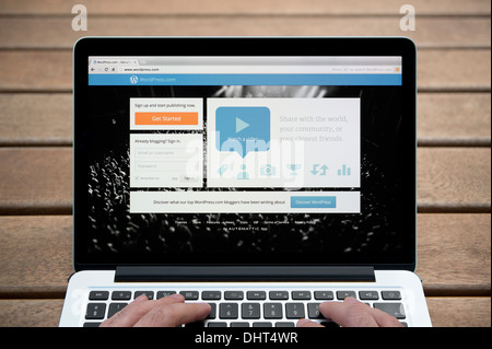 Il sito web di WordPress su un MacBook contro una panca in legno sfondo all'aperto tra cui un uomo le dita (solo uso editoriale). Foto Stock