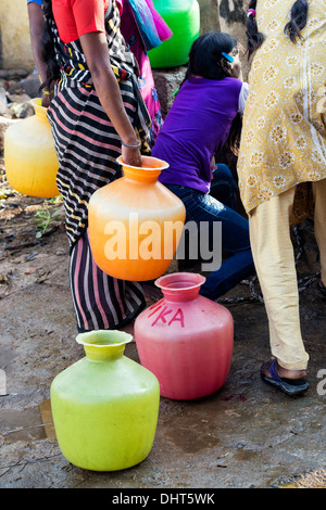 Vasi di plastica e donna indiana e ragazze in un pozzo di acqua in una zona rurale villaggio indiano street. Andhra Pradesh, India Foto Stock