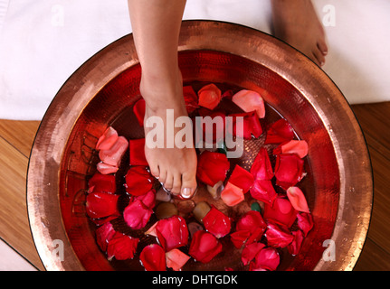 Donna di piedi nel bacino del riempimento con acqua e foglie di rose Foto Stock