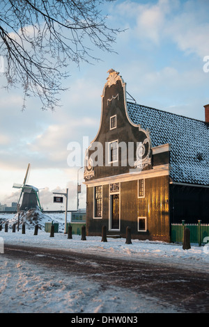 Paesi Bassi, Zaanse Schans, Zaandam, aria aperta di attrazione turistica. Mulini a vento e case. Inverno, Miller con zoccoli in bicicletta Foto Stock