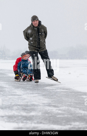 Paesi Bassi, Loosdrecht, laghi chiamato Loosdrechtse Plassen. L'inverno. Padre pattinaggio sul ghiaccio con figli su slitta Foto Stock