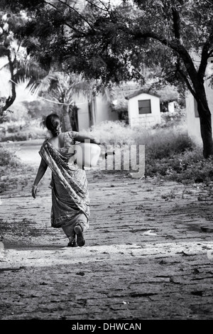 Donna indiana che porta un vaso in materia plastica con acqua da un tubo montante in un territorio rurale villaggio indiano street. Andhra Pradesh, India. In bianco e nero. Foto Stock