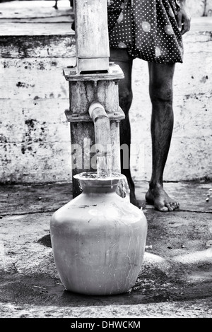 Uomo indiano il riempimento di una plastica pentola di acqua da un villaggio rurale la pompa a mano. Andhra Pradesh, India. Monocromatico Foto Stock