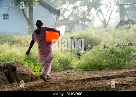 Donna indiana che porta un vaso in materia plastica con acqua proveniente da una pompa a mano in un territorio rurale villaggio indiano. Andhra Pradesh, India Foto Stock