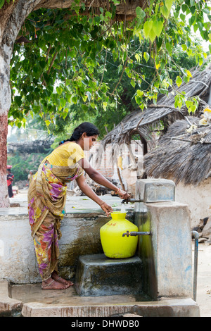 Donna indiana il riempimento di un contenitore di plastica con acqua da un tubo montante in un territorio rurale villaggio indiano street. Andhra Pradesh, India Foto Stock