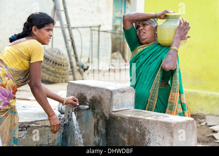 Le donne indiane il riempimento di bicchieri in plastica con acqua da un tubo montante in un territorio rurale villaggio indiano street. Andhra Pradesh, India Foto Stock