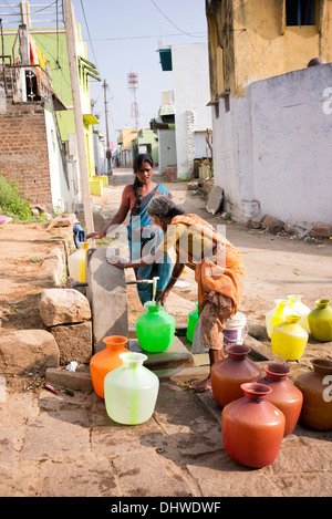 Le donne indiane il riempimento di bicchieri in plastica con acqua da un tubo montante in un territorio rurale villaggio indiano street. Andhra Pradesh, India Foto Stock