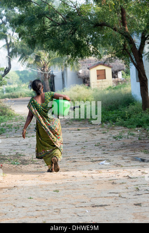 Donna indiana che porta un vaso in materia plastica con acqua proveniente da una pompa a mano in un territorio rurale villaggio indiano. Andhra Pradesh, India Foto Stock