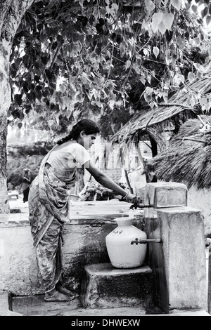 Donna indiana il riempimento di un contenitore di plastica con acqua da un tubo montante in un territorio rurale villaggio indiano street. Andhra Pradesh, India. In bianco e nero. Foto Stock