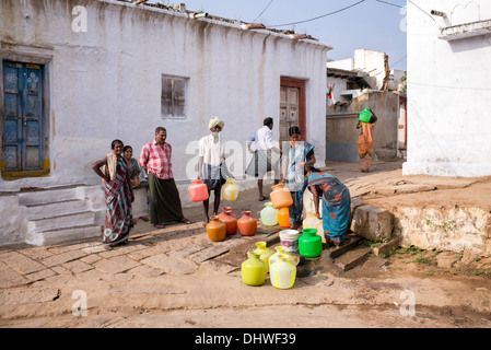 Le donne indiane il riempimento di bicchieri in plastica con acqua da un tubo montante in un territorio rurale villaggio indiano street. Andhra Pradesh, India Foto Stock