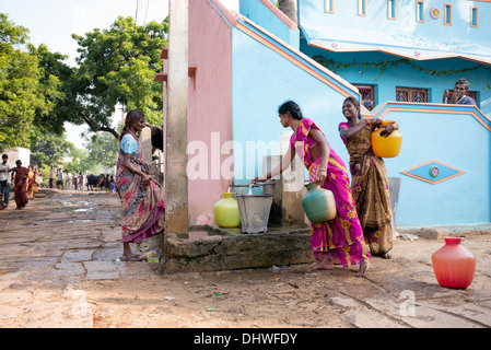 Le donne indiane il riempimento di bicchieri in plastica con acqua da un tubo montante in un territorio rurale villaggio indiano street. Andhra Pradesh, India Foto Stock