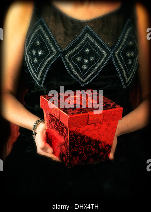 Una donna tagliata in un periodo dress tenendo un elegante confezione regalo rossa Foto Stock