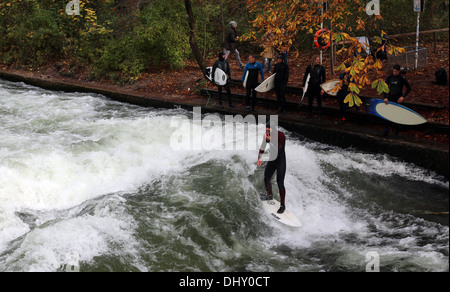 Surfers treno su una man-made ondata di circa 1 metro di altezza nel fiume Eisbach nel Giardino Inglese a Monaco di Baviera, Germania Foto Stock