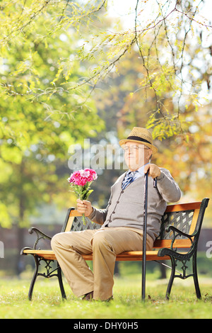 Senior gentleman con bouquet di fiori seduta su una panchina in un parco Foto Stock