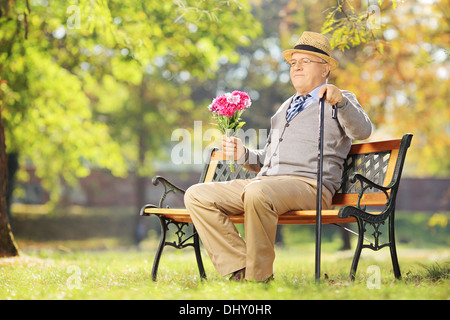 Senior gentleman con mazzo di fiori in seduta su una panchina in un parco Foto Stock