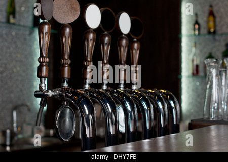 Vista attraverso il contatore di una fila di rubinetti di birra su un acciaio inox meccanica barile in un pub usato per erogare la birra alla spina Foto Stock