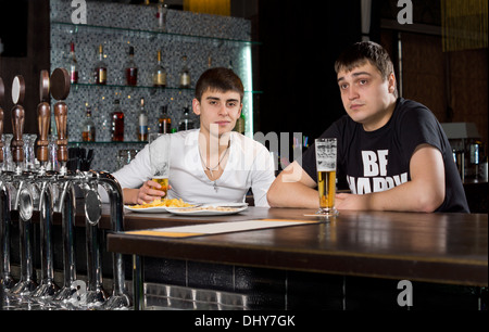 Due giovani uomini adolescenti bere al pub seduto al bancone del bar godendo di una pinta di birra Foto Stock