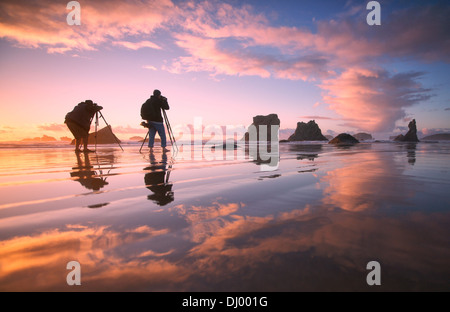 Due fotografi di scattare le foto delle formazioni rocciose sulla spiaggia di Bandon, Oregon Coast al tramonto Foto Stock