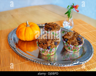 Tre zucca chocolate chip muffin su un argento piatto di portata con una piccola zucca decorativa e un vaso di fiori. Foto Stock