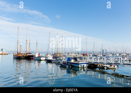 Pontile bianco passerella che conduce a barche e yacht in un marina con cielo blu e riflessi Foto Stock