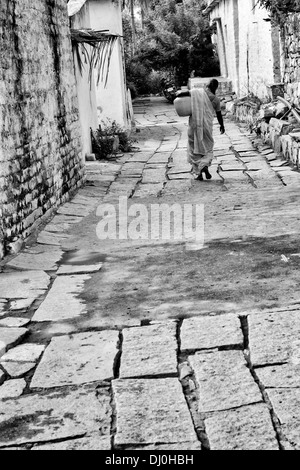 Donna indiana che porta un vaso in materia plastica con acqua da un tubo montante in un territorio rurale villaggio indiano street. Andhra Pradesh, India. In bianco e nero. Foto Stock