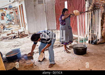 Un zapoteco donna indigena mano fa di candele in cera d'api come suo figlio riscalda una vasca di cera per il Giorno dei Morti festival noto in spagnolo come Día de Muertos Ottobre 30, 2013 in Teotitlan, Messico. Foto Stock