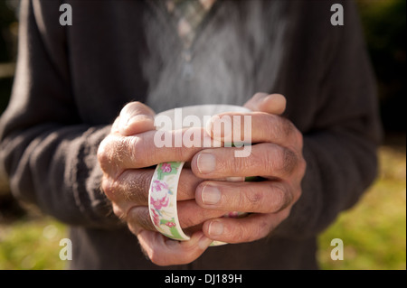 In fase di riscaldamento a freddo con le mani una fumante tazza di tè dopo il giardinaggio sulla soleggiata freddo giorno d'autunno Foto Stock