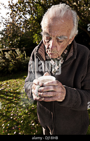 In fase di riscaldamento a freddo con le mani una fumante tazza di tè dopo il giardinaggio sulla soleggiata freddo giorno d'autunno Foto Stock