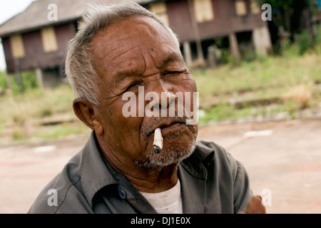 Un anziano uomo tailandese è di fumare a casa sigaretta arrotolata in un abondoned raildroad stazione in Nong Khai (Kai) Thailandia. Foto Stock