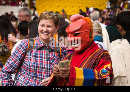 Il Bhutan, Thimpu Dzong, annuale Tsechu femmina turista occidentale con atsara clown ballerina azienda soldi in mano Foto Stock