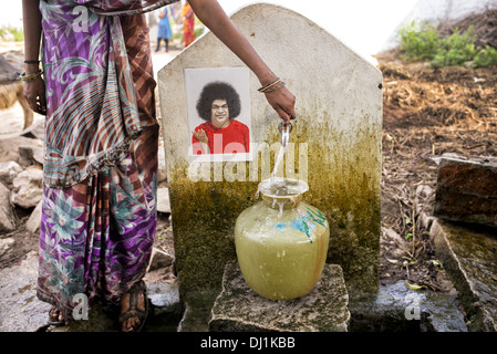 Le donne indiane il riempimento di un contenitore di plastica con acqua da un tubo montante in un territorio rurale villaggio indiano street. Andhra Pradesh, India Foto Stock