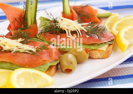 Panini con salmone, formaggio, lattuga, erbe su piastra, olive e limoni. Foto Stock