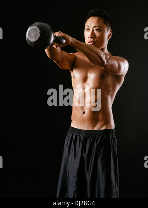 Foto di un maschio asiatici esercitando con un bollitore bell su sfondo scuro. Foto Stock