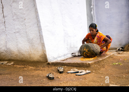 Donna indiana utilizzando una pietra per macinare gli ingredienti per fare il chutney al di fuori del suo villaggio rurale casa. Andhra Pradesh, India Foto Stock