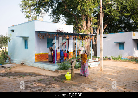 Donna indiana di riempimento acqua in plastica vaso da un villaggio rurale la pompa a mano. Andhra Pradesh, India Foto Stock