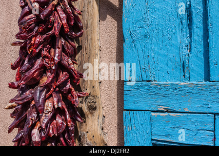 Un rosso peperoncino pende ristra essiccazione al sole su una parete di adobe accanto a una luce blu weathered porta in legno a Santa Fe, N.M. Foto Stock