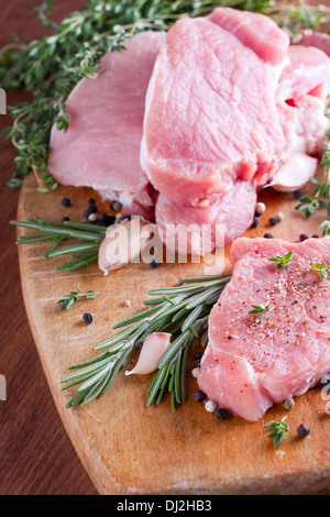 Pezzi di carne di maiale cruda con aglio e rosmarino sul pannello di legno Foto Stock