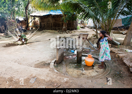 Ragazza indiana di riempimento acqua in plastica vaso da un villaggio rurale la pompa a mano. Andhra Pradesh, India Foto Stock