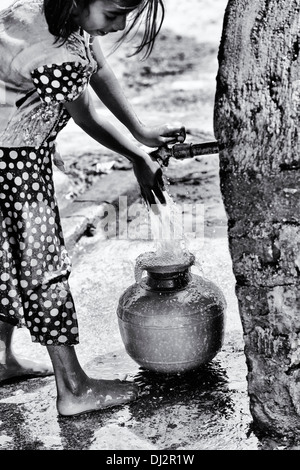 Ragazza indiana il riempimento di un contenitore di plastica con acqua da un tubo montante in un territorio rurale villaggio indiano. Andhra Pradesh, India. In bianco e nero. Foto Stock